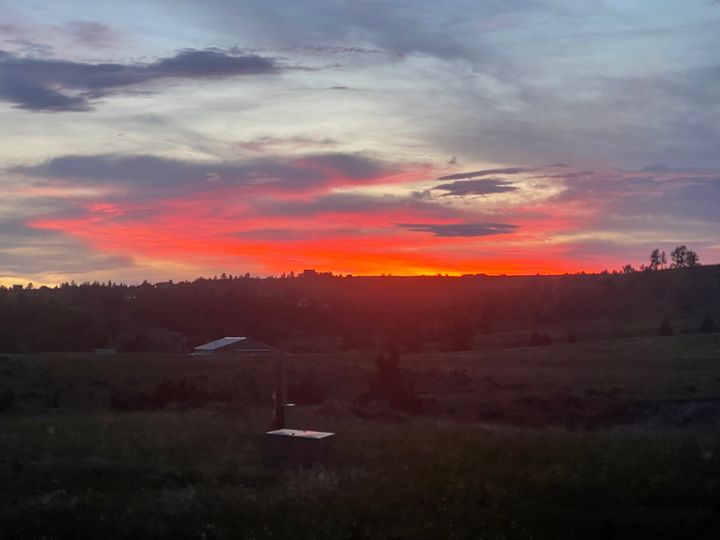 An orange red sunset with clouds, overtop a dark prairie land